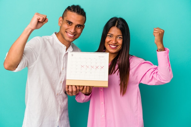 Jeune couple latin tenant un calendrier isolé sur mur bleu