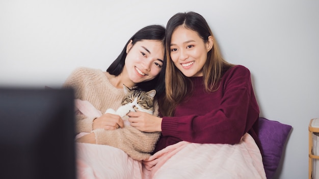 Jeune couple de lesbiennes belles femmes asiatiques regardant la télévision avec chat ensemble dans la chambre à coucher.