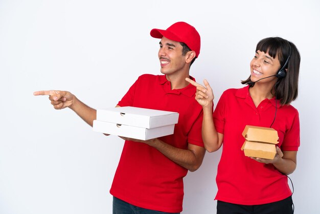 Jeune couple de livraison tenant des pizzas et des hamburgers isolés sur fond blanc tendant les mains sur le côté pour inviter à venir