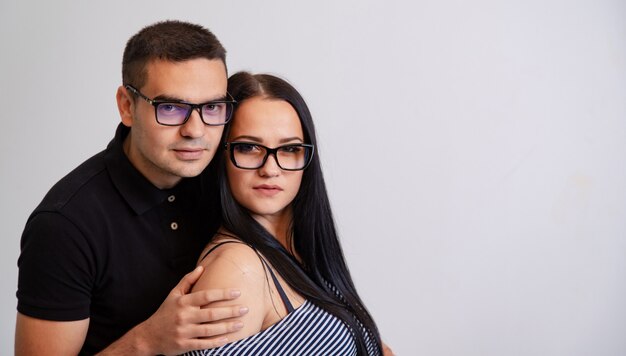 Jeune couple en lunettes modernes. L'homme embrasse la femme. Arrière-plan blanc flou. Garçon et fille à lunettes. Brune aux cheveux longs. Belle femme et bel homme.