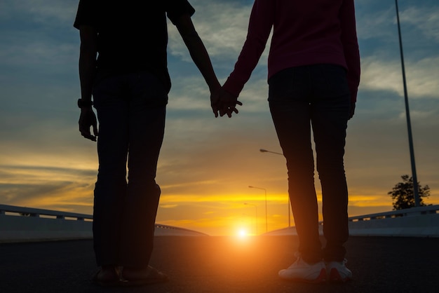 Jeune couple main dans la main sur la route au coucher du soleil.