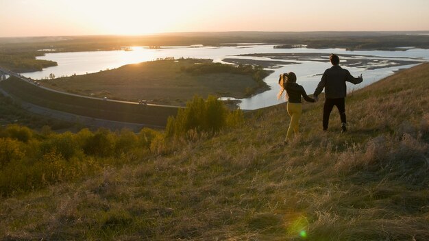 Jeune couple marchant dans un champ main dans la main au coucher du soleil se bouchent