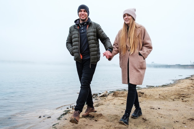 Un jeune couple marche le long de la rive du lac et se tient la main - Un couple marié marche le long de la rive et communique gentiment