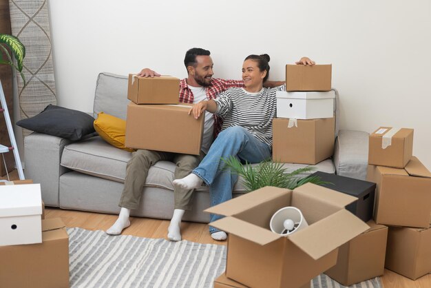 Un jeune couple marié sur le canapé entouré de boîtes en carton épuisé mais ravi après le déménagement