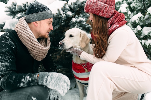 Jeune couple marié caressant leur chien dans une rue enneigée assis à côté d'elle