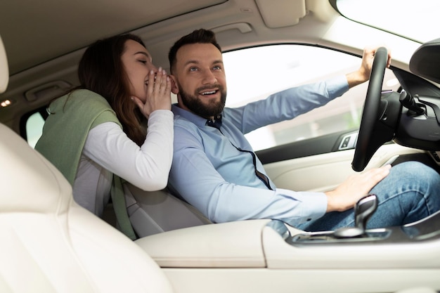 Un jeune couple marié dans un concessionnaire automobile choisit une nouvelle voiture en chuchotant entre eux