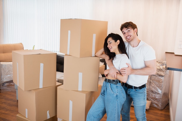 jeune couple marié dans le salon de la maison se tient près des boîtes déballées. ils sont contents de leur nouvelle maison. Déménagement, achat d'une maison, concept d'appartement.