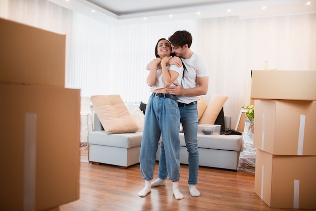 jeune couple marié dans le salon de la maison se tient près des boîtes déballées. ils sont contents de leur nouvelle maison. Déménagement, achat d'une maison, concept d'appartement.