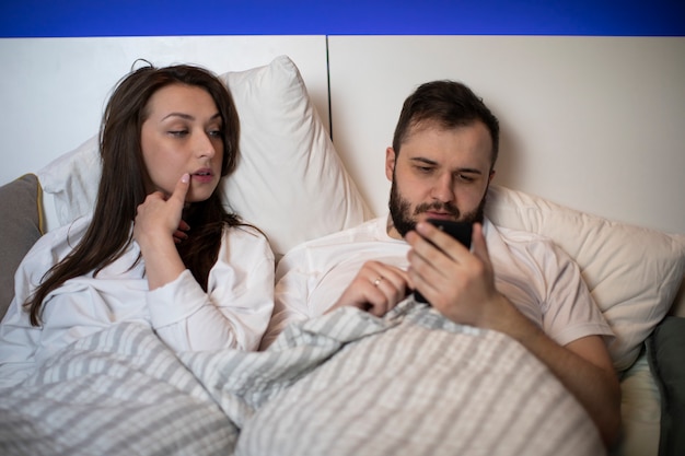 Jeune, couple marié, pose, dans lit, homme, utilisation, téléphone portable, ignorer, sien, épouse