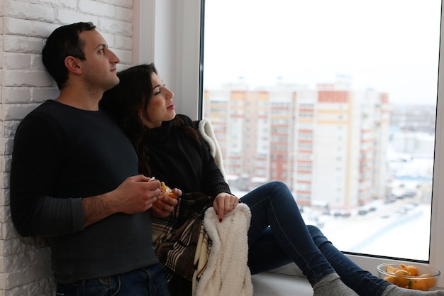 Un jeune couple marié regarde par la fenêtre d'un nouvel appartement