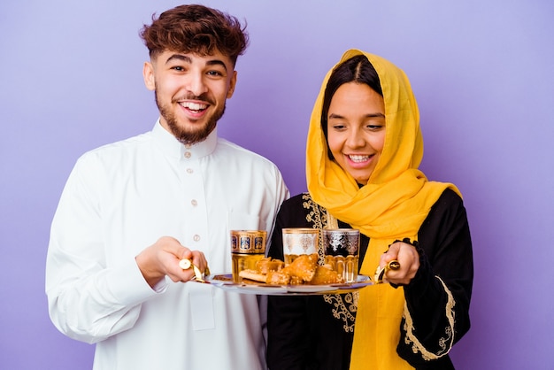 Jeune couple marocain buvant du thé célébrant le mois du ramadan isolé sur fond violet