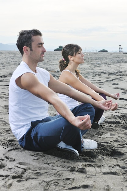 jeune couple méditant le yoga en position du lotus tôt le matin sur la plage