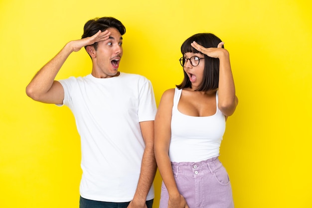 Jeune couple métis isolé sur fond jaune avec une expression faciale surprise et choquée