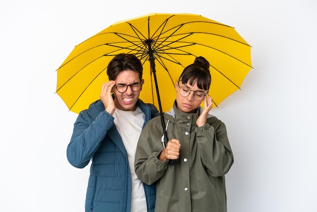 Jeune couple métis tenant un parapluie isolé sur fond blanc malheureux et frustré par quelque chose