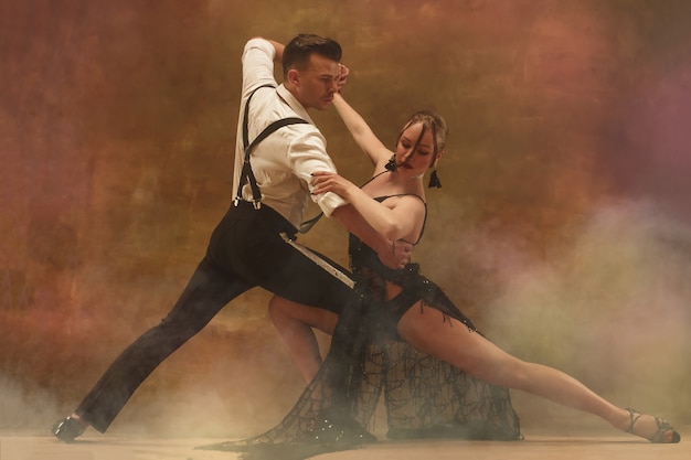 Photo jeune couple moderne flexible dansant le tango en studio. mode portrait d'un couple de danseurs attrayant. homme et femme. la passion. amour. peau parfaite du visage et maquillage. émotions humaines - amour et passion