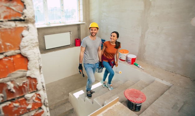 Jeune couple moderne et heureux amoureux de vêtements décontractés lors de la réparation d'une nouvelle maison ou de la rénovation des murs avec beaucoup d'outils pour cela