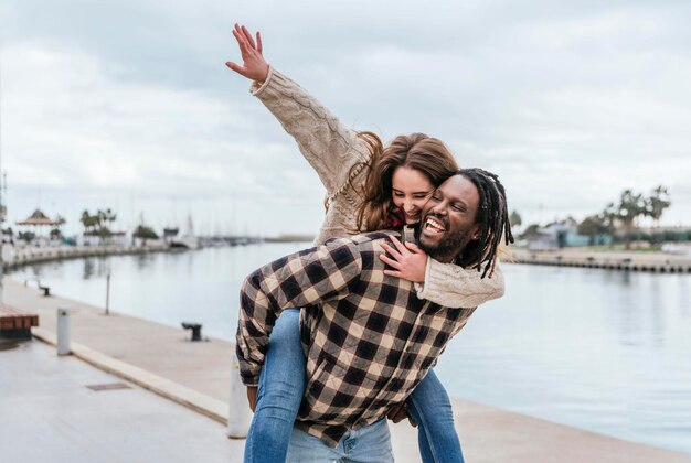 Jeune couple multiethnique ayant une faune à l'extérieur, le gars donne à sa petite amie un tour de ferroutage