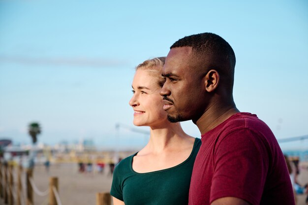 jeune couple multiethnique à la plage à la recherche de l'appareil photo avec copie espace