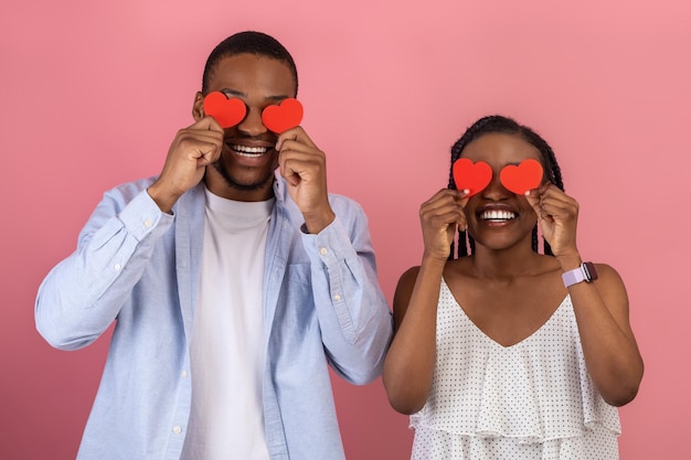 Jeune couple noir romantique couvrant les yeux avec des coeurs en papier rouge