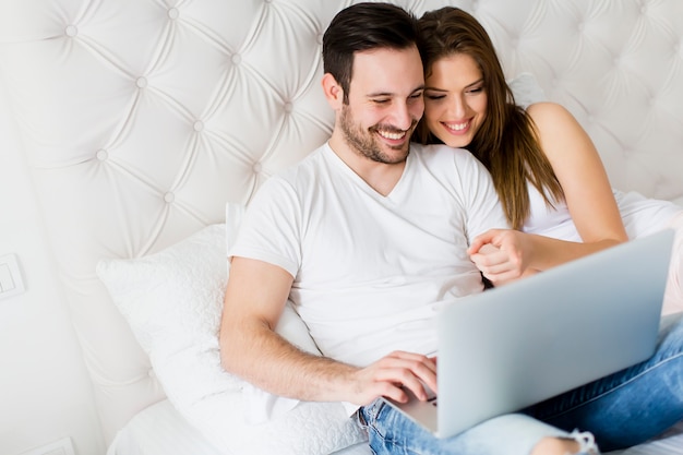 Jeune couple avec ordinateur portable dans le lit