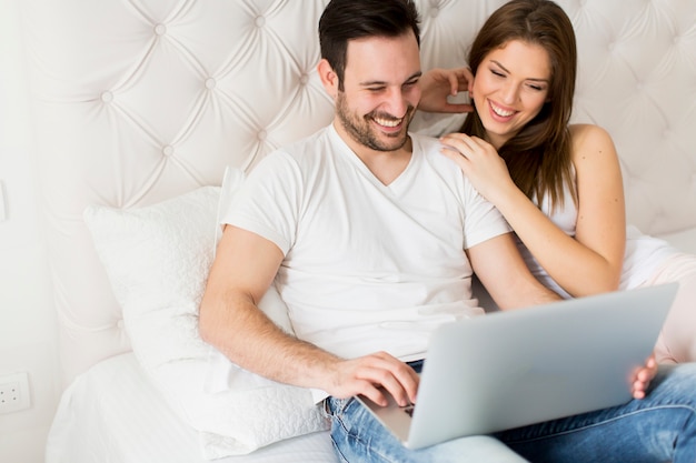 Jeune couple avec ordinateur portable dans le lit