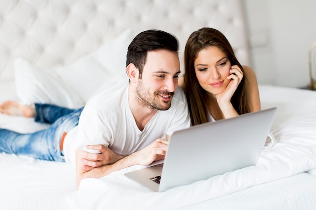 Jeune couple avec ordinateur portable dans le lit