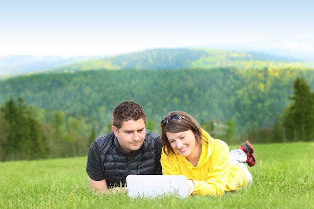 un jeune couple et un ordinateur portable sur l'herbe dans les montagnes