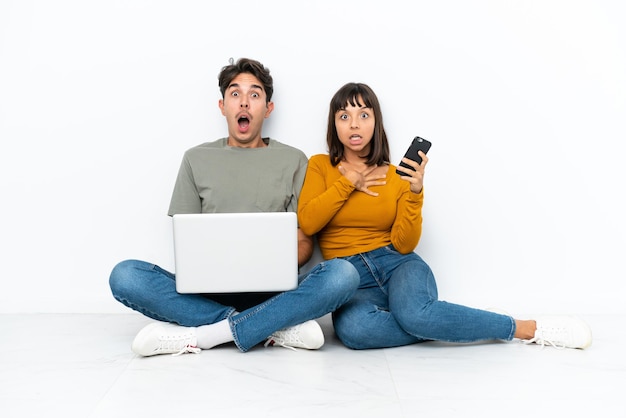 Jeune couple avec un ordinateur portable et un téléphone portable assis sur le sol