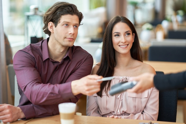 Jeune couple payant par carte de crédit au café