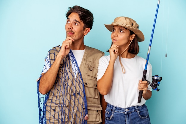 Jeune couple de pêcheurs métis isolé sur fond bleu regardant de côté avec une expression douteuse et sceptique.