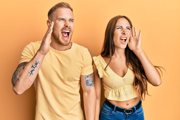 Jeune couple de petite amie et petit ami étreignant et debout ensemble criant et criant fort à côté avec le concept de communication main sur bouche