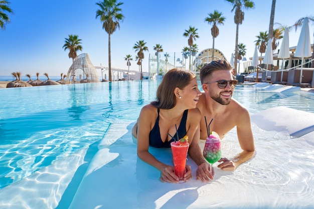 Jeune couple sur la piscine à débordement avec des cocktails