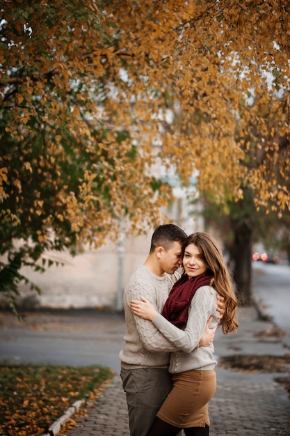 Jeune couple portant des chandails chauds attachés étreignant amoureusement à la ville en automne.