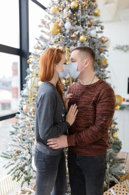 jeune couple portant des masques médicaux près de l'arbre de Noël. malade contagieux