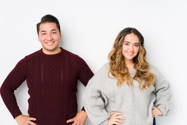 Jeune couple posant dans un mur blanc confiant en gardant les mains sur les hanches.