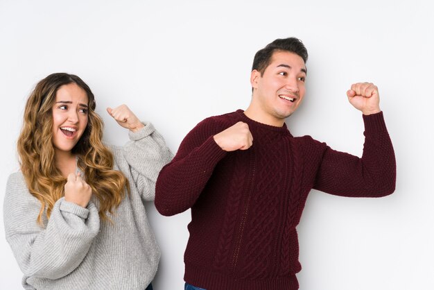 Jeune couple posant dans un mur blanc levant le poing après une victoire, concept gagnant.