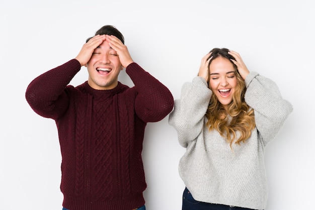 Jeune couple posant dans un mur blanc rit joyeusement en gardant les mains sur la tête. Concept de bonheur.