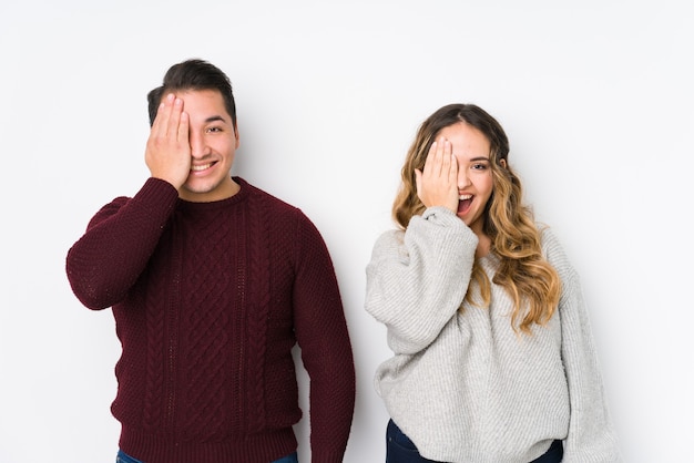 Jeune couple posant dans un mur blanc s'amusant couvrant la moitié du visage avec la paume.