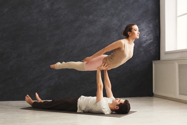 Jeune couple pratiquant l'acroyoga sur tapis dans une salle de sport ensemble. Femme volant, copiez l'espace. Yoga partenaire, flexibilité, concept de confiance