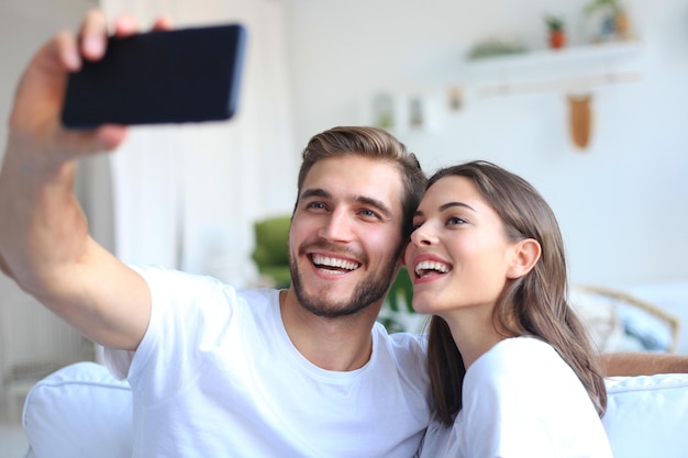 Jeune couple prenant un selfie sur canapé à la maison dans le salon.