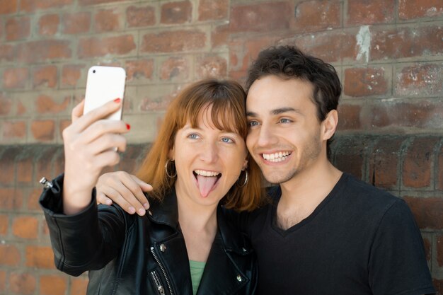 Photo jeune couple prenant selfie avec un téléphone mobile à l'extérieur.