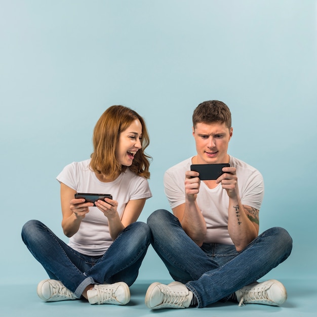 Jeune couple de profiter du jeu vidéo sur téléphone portable dans le contexte bleu