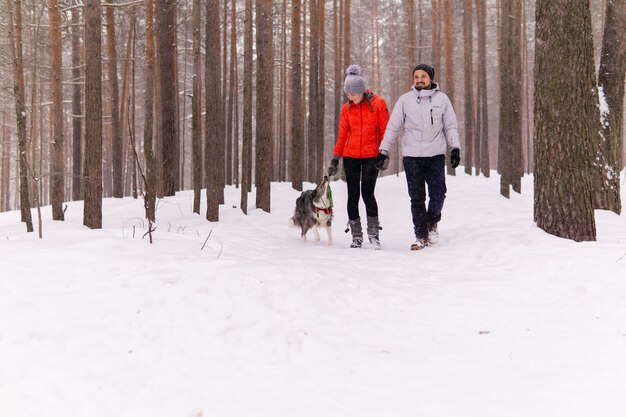 Jeune couple promenant un chien dans une forêt d'hiver enneigée, le chien veut jouer