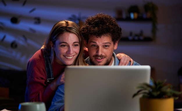 Un jeune couple qui utilise un ordinateur portable à la maison pendant la nuit à la recherche d'une destination de voyage