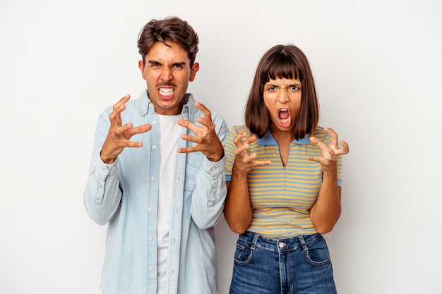 Jeune couple de race mixte isolé sur fond blanc contrarié de crier avec les mains tendues.