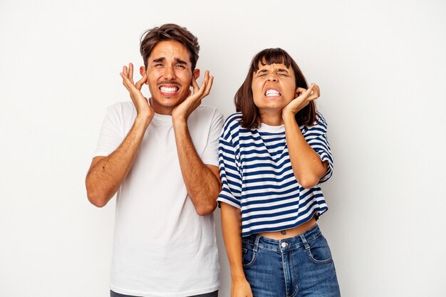 Jeune couple de race mixte isolé sur fond blanc couvrant les oreilles avec les mains.