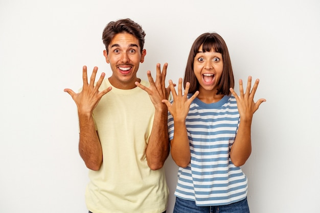 Jeune couple de race mixte isolé sur fond blanc montrant le numéro dix avec les mains.