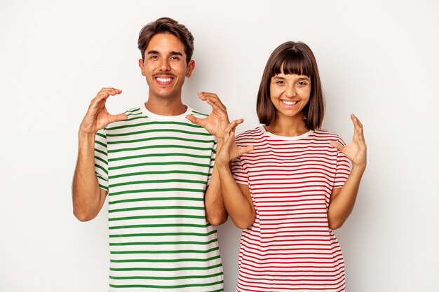 Jeune couple de race mixte isolé sur fond blanc tenant quelque chose avec des palmiers, offrant à la caméra.