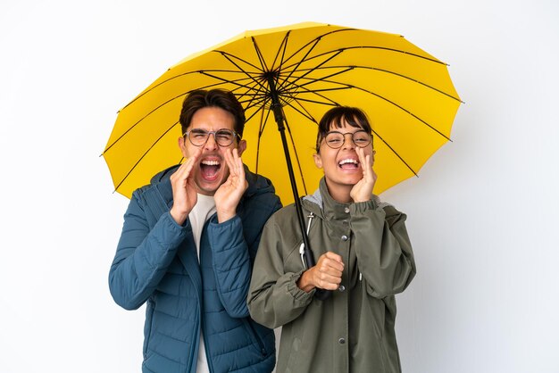 Jeune couple de race mixte tenant un parapluie isolé sur fond blanc criant et annonçant quelque chose