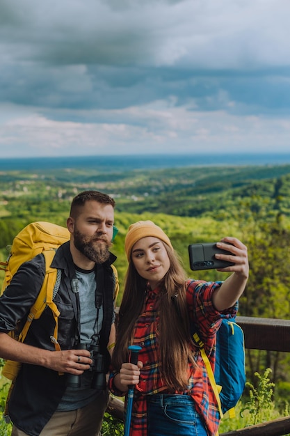 Jeune couple de randonneurs debout à l'affût et prenant un selfie avec un smartphone